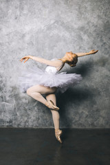 Obraz na płótnie Canvas Pretty young ballerina dancer dancing classical ballet against rustic wall