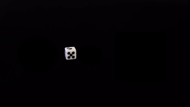 One white dice flies out on a black background. Playing cube flies, rotates on a black surface. Stops in sight. Concept of business and casino or gambling. Close-up.