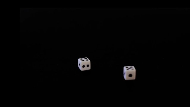 Dice fall in turn, white cubes fly out on a black background. Cubes fall, rotate on a black surface. Stops in sight. Concept of business, casino or gambling. Close-up.
