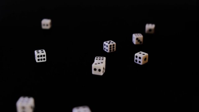 White cubes fall out, fly out on a black background for the game. Dice fall, rotate and bounce on a black surface. Stops in sight. Concept of business and casino or gambling. Close-up.