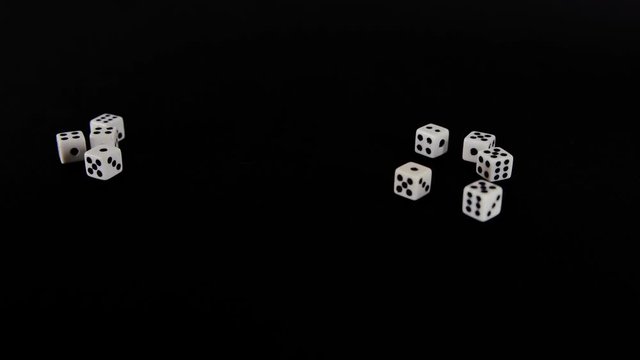 White cubes fly out on a black background. The dice rotate on a black surface. Stops in sight. Concept of business and casino or gambling. Close-up.