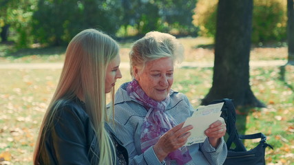 Close-up shot of old woman reading a letter to pretty young woman in park. She reading some interesting story of her life.