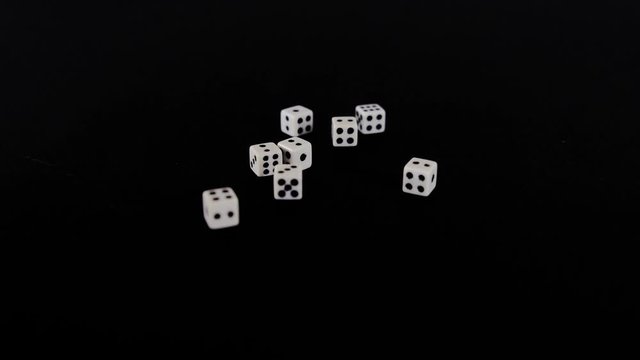From two sides white cubes fly out on a black background. The dice rotate on a black surface. Stops in sight. Concept of business and casino or gambling. Close-up.