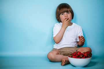 Toddler boy sitting with bowl of strawberries on the blue background