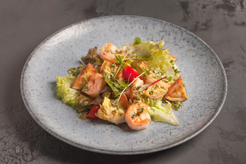 Restaurant menu. Warm salad with tomatoes, king prawns, eggplant and lettuce. Micro-village. Blue plate.Red, orange, green, yellow