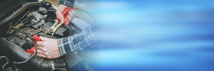 Hands of car mechanic using car battery jumper cable; panoramic banner