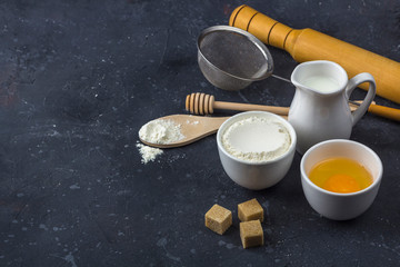 Baking background. Ingredients and utensils for cooking cake (flour, egg, milk, sugar, rolling pin, wooden spoon) on dark table. Food concept. Close up layout, copy space for text.
