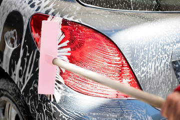 Man's hand with pink brush washing gray car. © Evgeniia