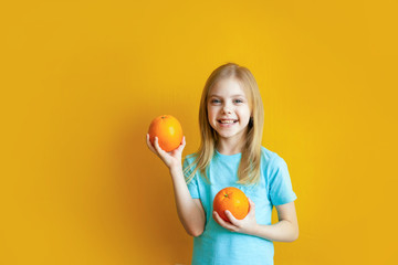 Cute baby 8 years old on an orange background, blonde pretty girl with appelsins in her hands smiles