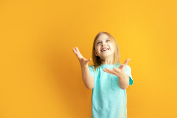 cute baby on an orange background, 6-8 years old, baby girl catches something or is ready to catch falling from above