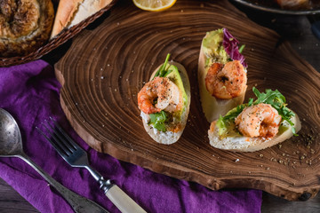 Fototapeta na wymiar Sandwiches with shrimp, cheese and avocado on a wooden tray on the table, dark background. The concept of nutrition and beautiful serving of food