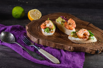 Sandwiches with shrimp, cheese and avocado on a wooden tray on the table, dark background. The concept of nutrition and beautiful serving of food