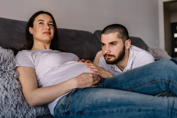 Portrait of a happy pregnant woman holding baby shoes and of her husband on a sofa at home