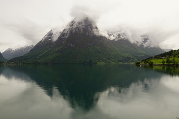Reflections of misty mountains in the waters of Oppstrynsvatn lake in Norway
