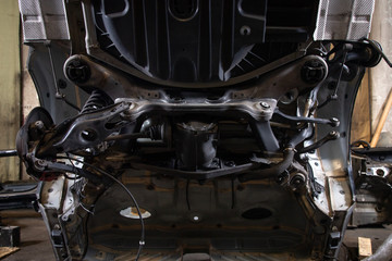 Fototapeta Close-up, sawn off part of an old car body: underbody, multi-link rear suspension, disc brakes, suspension arms, brake pipes in an old garage. Parsing jankyard obraz