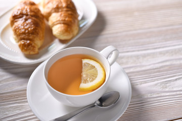 Top view of a cup of tea with lemon and croissant on white table