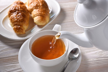 Pouring hot tea into a cup on white table background