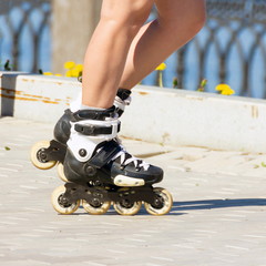 Beautiful female legs in roller skates on the embankment of the river on a summer sunny day.