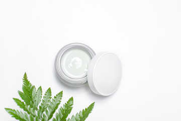 Cosmetic cream in container and fresh green leaves on white background. Homemade spa, jar of...
