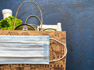 Paper bag with food, antiseptic and medical mask on a blue background. Food delivery, donation....