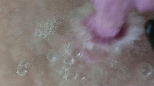 Close up pouring pink pulp into water for paper making, gloved hand stirring the water.