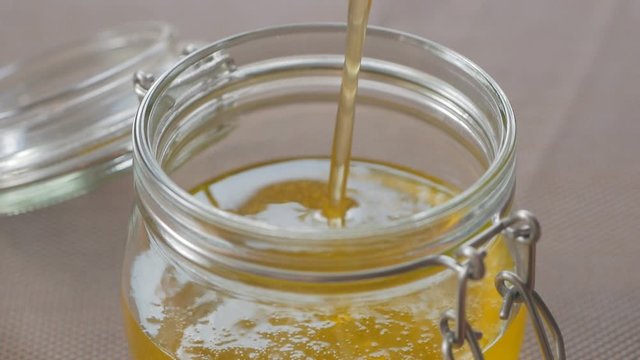 Close-up of pouring clarified butter ghee in a glass jar for storage