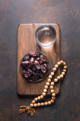Ramadan. Dates in bowl, glass of water, wooden prayer beads on brown. Eid Mubarak. Religious tradition. Vertical .