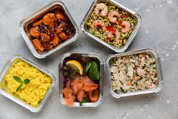 Food delivery. Different aluminium lunch box with healthy food risotto, chicken with chickpeas and rice, salmon and spinach, chicken teriyaki, shrimp and green beans. airline meals snacks. takeaway