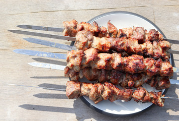 Grilled shish kebab on skewers on a white round plate on a aged wood background. Top view, flat lay
