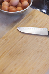 A sharp knife on a wooden board with a bowl of eggs on a table in the kitchen