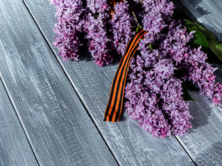 Lilac with St. George's ribbon on a wooden background. Flowers in memory of Soviet soldiers who died during the great Patriotic war. May 9, Victory Day.