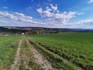Erzgebirge, Feld im Frühling mit Blick auf Häusern bei strahlend blauem Himmel und ein paar Wolken