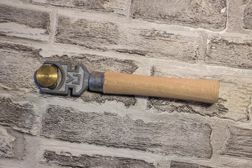 Manual glass cutter with a wooden handle on a brick wall background.