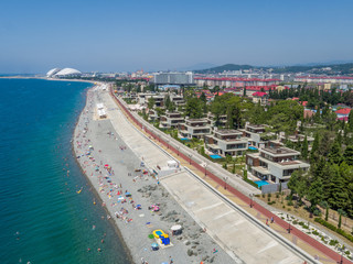 People on the beach. Sea, coastline, beach umbrellas, promenade and luxury homes. Aerial view.