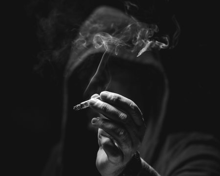 Persona encapuchada en la sombra fumando