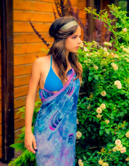 Beautiful young woman posing against a backdrop of greenery and a bungalow with a blue tissue. Elegant girl with scarf and bijouterie enjoying at beach. Freedom and carefree concept, Bali. tanning