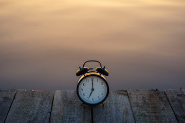 Summer time concept. Alarm clock on wooden bridge on sea sunrise background