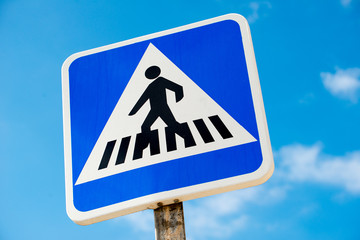 Low angle view of Spanish pedestrian crossing road sign, against a background of blue sky with small clouds.