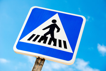Low angle view of Spanish pedestrian crossing road sign, against a background of blue sky with small clouds.