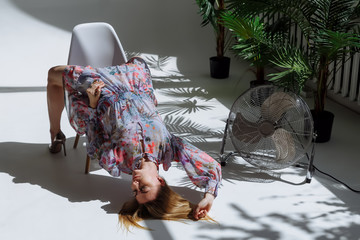 A girl in a light dress lies on the floor in an unusual position, leaning on a chair. Fashion...