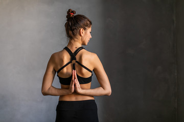 Young women meditating with namaste mudra sign at yoga class. Hands clasped behind her back. Yoga stretch exercise on dark background.