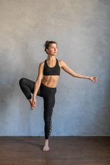 Fototapeta na wymiar Young woman standing in a yoga exercise position. Girl balancing, practice stretch exercise at yoga class - she is standing on one leg