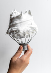 Hand holding whisk with whipped cream
