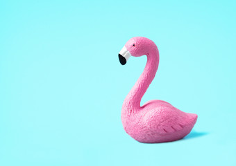 Closeup of a small pink toy flamingo isolated on a light blue background. Summer vacation concept. Low angle, side view.