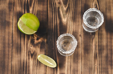 Tequila shots with lime slices and salt on wooden table/Tequila shots and lime slice on wooden table. Top view