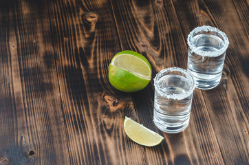 two Tequila shots with lime slices and salt on wooden table/Tequila shots and lime slice on wooden table with Copy cpace. Top view.