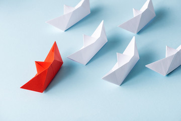 Fototapeta premium High angle view of unique red paper boat among white on blue