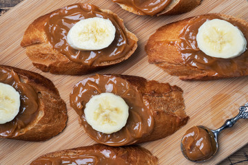 Sandwiches with baguette of bread spread with sweet paste of boiled condensed milk and banana. Wooden background.
