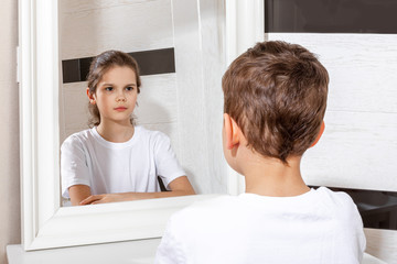 Reflection of a boy in the mirror by a girl. Sister and brother concept. Boy and girl. Concept of Gender dysphoria. - obrazy, fototapety, plakaty