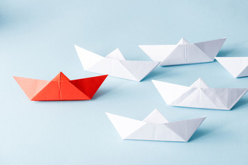 Unique red paper boat among white on blue background